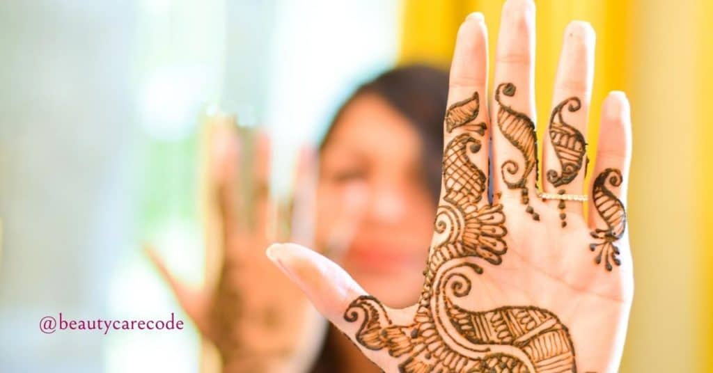 An image of a hand decorated with henna in a blurry background of a woman's face to show the benefits and disadvantages of henna for hair