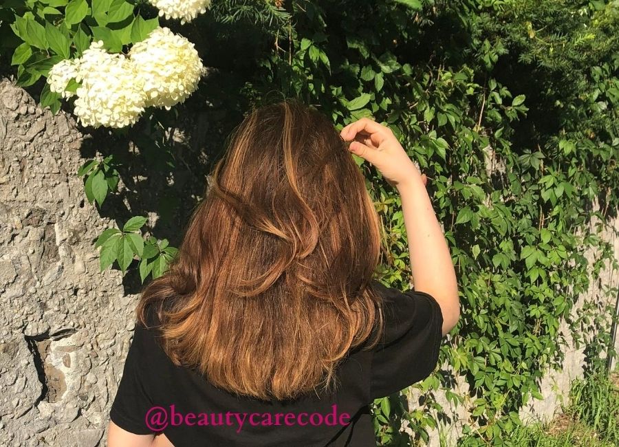An image of a girl with shiny nice hair from the back with flower and plants outdoor to discuss home remedy for dandruff