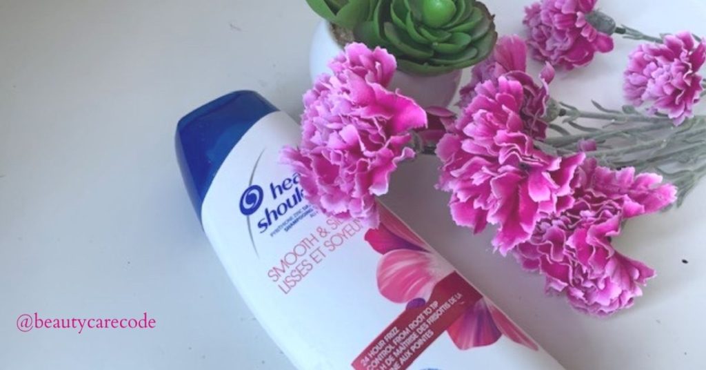 An image of a shampoo for dandruff with pink flowers and a green plant in small white vase.