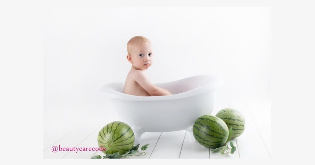 An image of a baby in a white bath tub with a few watermelon around in white background