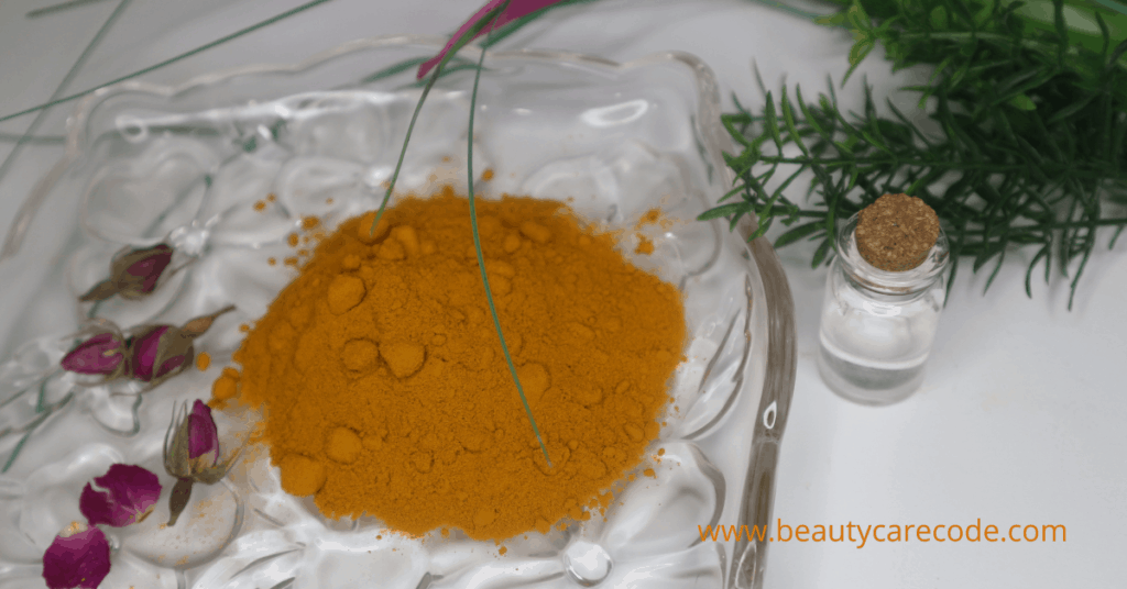 An image of turmeric powder in a glass plate with t a few dried rose and herbs in white background
